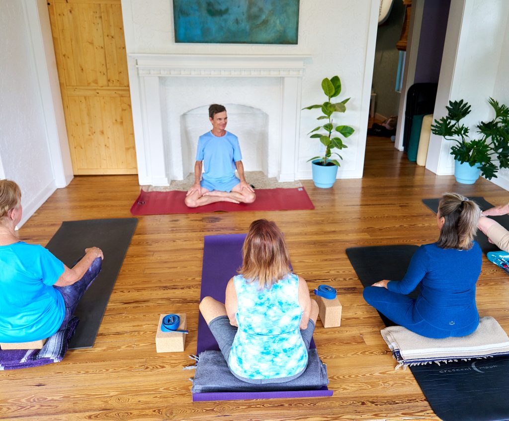 Instructor guiding students through a yoga session in a bright, calm studio.